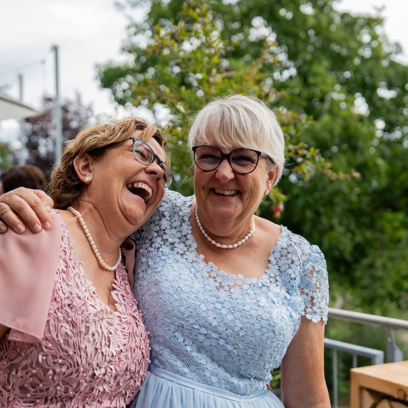 Zwei G&auml;ste lachen Arm in Arm beim Ap&eacute;ro